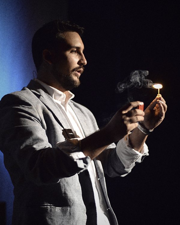 Javier Natera, bilingual mentalist for corporate events in Mexico, holding a small flame under blue stage light