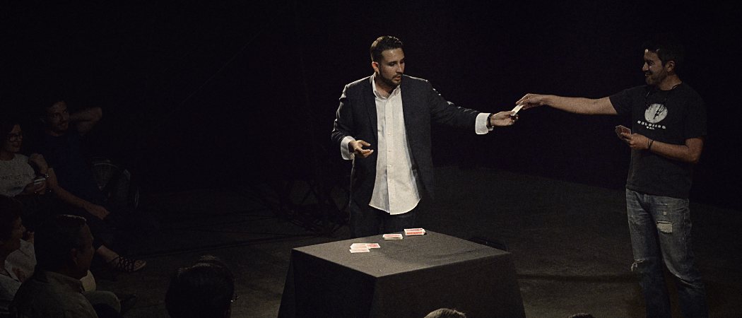 Javier Natera en el escenario junto a un participante del público, con los asistentes alrededor
